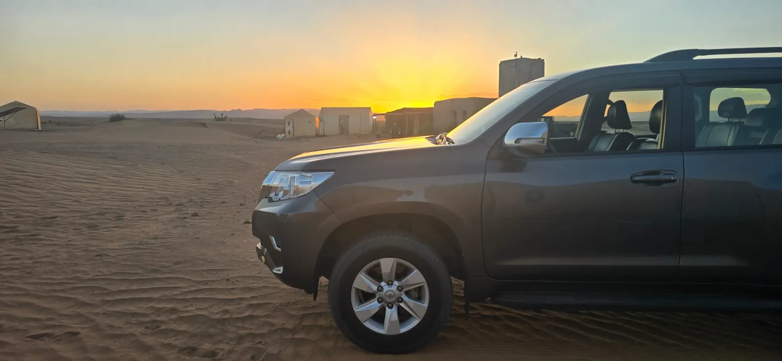 4x4 SUV parked at Sahara desert camp during golden hour sunset